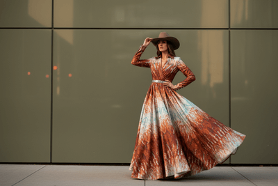 Woman in a long, patterned dress standing against a reflective wall.